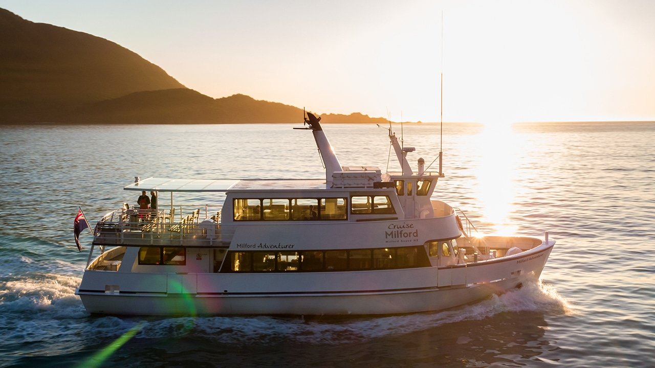 Large cruise boat navigating the stunning fjords of Milford Sound with towering cliffs