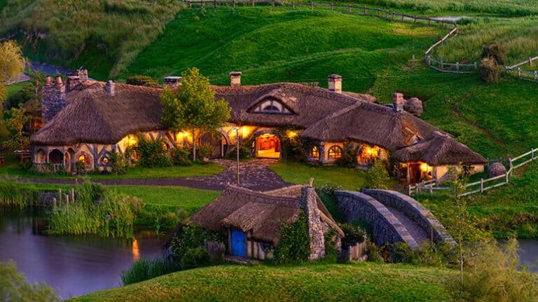 Arched stone bridge at Hobbiton with lit-up hobbit homes at twilight