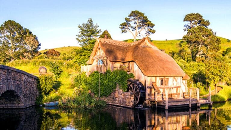 Hobbiton lake with hobbit homes, arched bridge, and water wheel in view