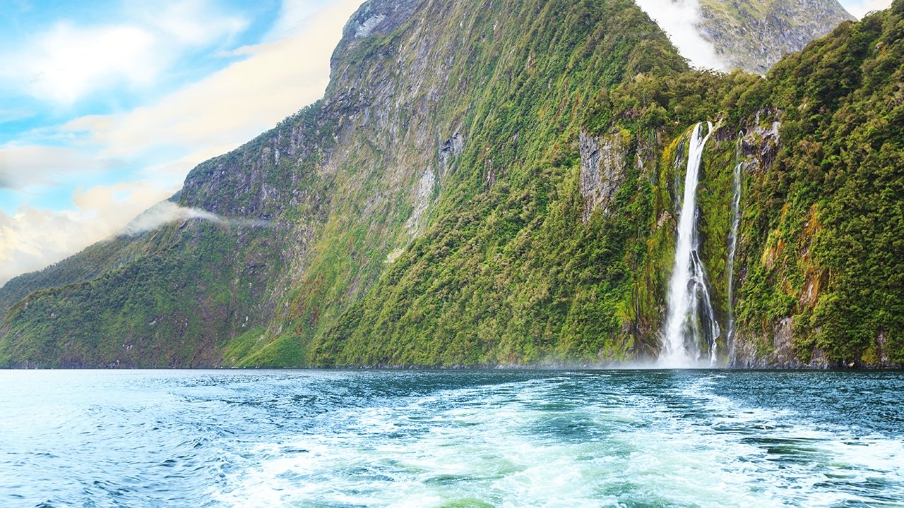 Waterfalls cascading down rugged, steep mountains into the fjord waters of Milford Sound