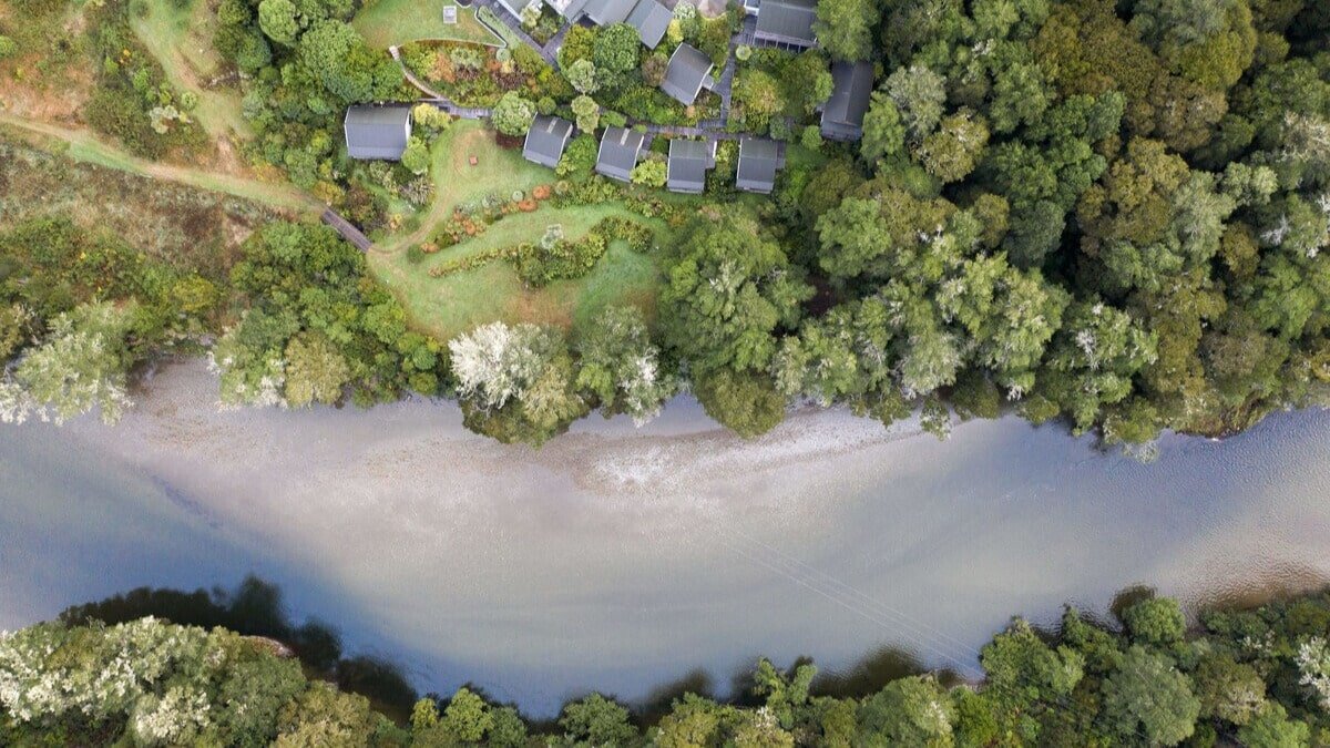 Aerial view of Maruia River Retreat bordered by the river and surrounded by lush rainforest