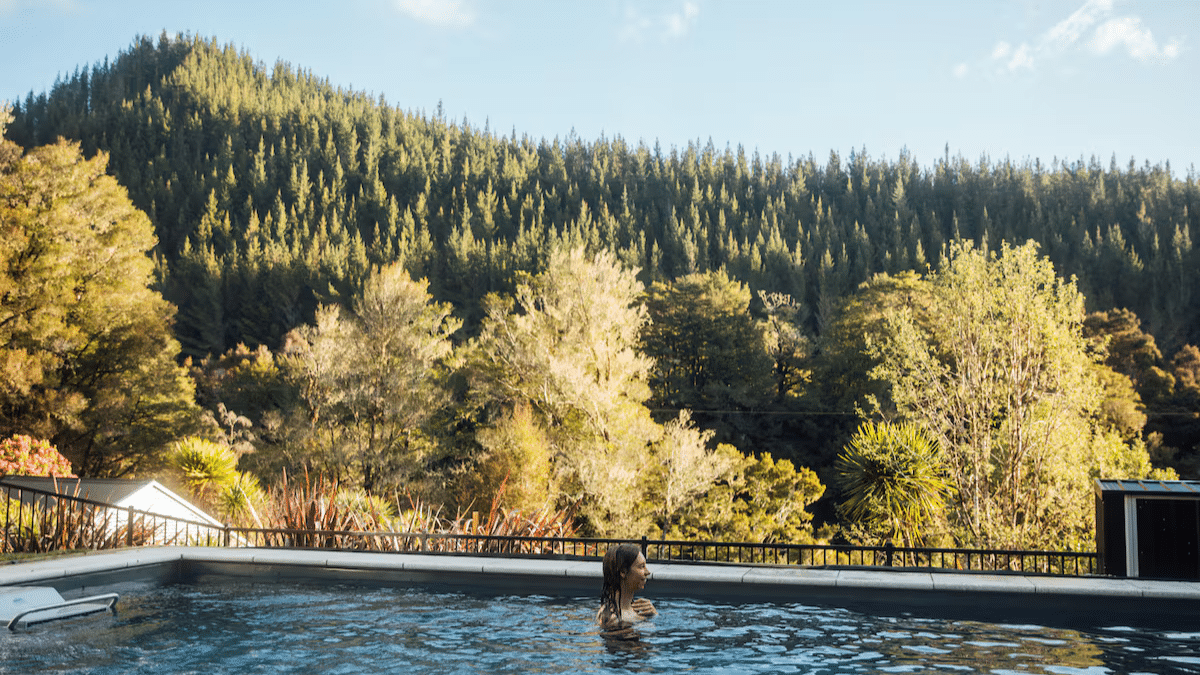 Person swimming in the heated magnesium pool at Maruia River Retreat surrounded by lush rainforest