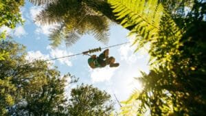 Person ziplining high above native bush with expansive sky views at Okere Forest