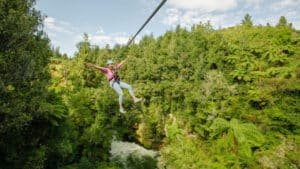 Person ziplining through native bush with arms outstretched enjoying the Okere Forest zipline ride