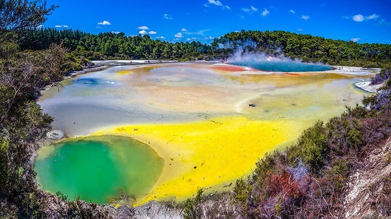 Brightly coloured geothermal pools in green, blue, yellow and orange hues with rising steam at Wai-O-Tapu in Rotorua