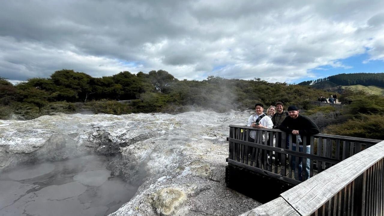 Visitors on a viewing platform watching bubbling mud pools and steam vents at Wai-O-Tapu geothermal area