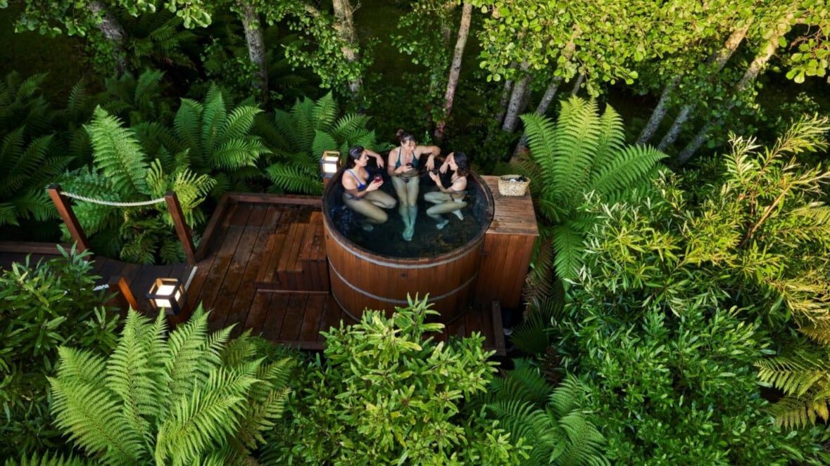 Group of friends relaxing together in a private hot tub surrounded by lush native forest in Rotorua