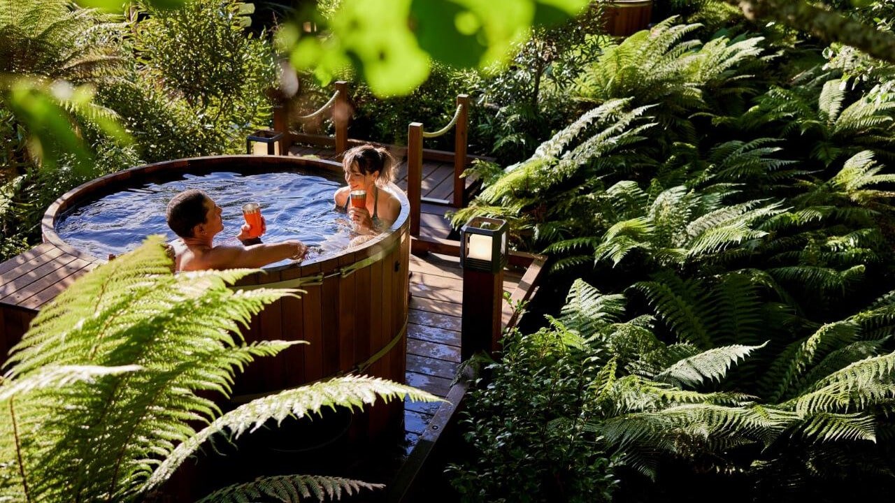 Couple relaxing and enjoying drinks together in a private hot tub surrounded by lush native nature in Rotorua