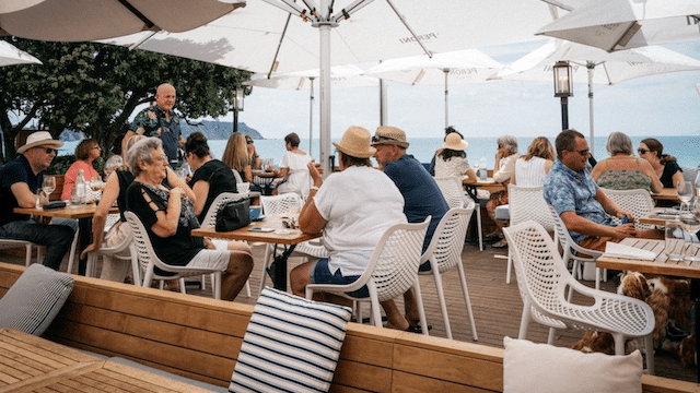 Guests seated outdoors enjoying lunch under sun umbrellas on Waiheke Island wine tour