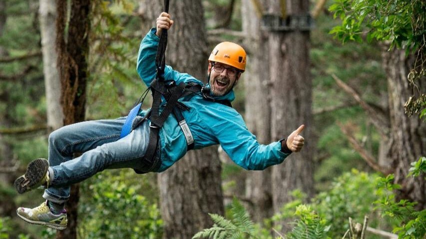 Person giving thumbs up while ziplining through native bush in Coromandel