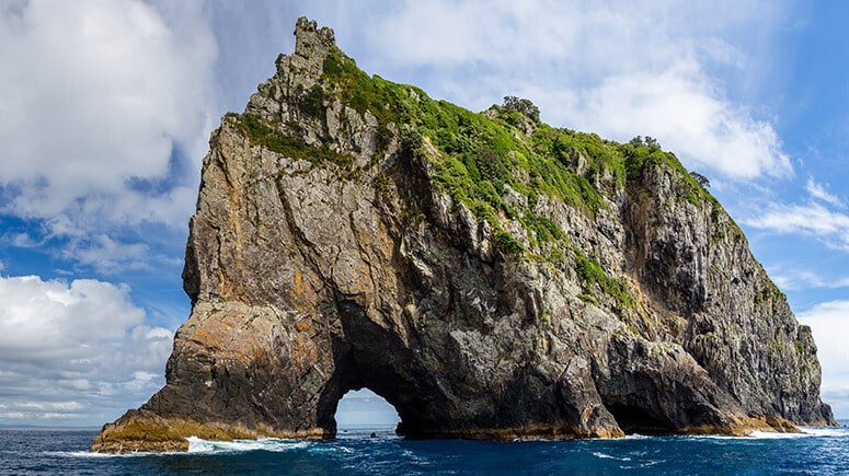 The iconic Hole in the Rock formation surrounded by blue sea waters in the Bay of Islands.
