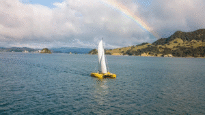 Catamaran sailing in the Bay of Islands with a vibrant rainbow arching in the background over the coastline.