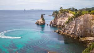Boat cruising in the calm, turquoise waters of a picturesque bay near Cathedral Cove, Coromandel