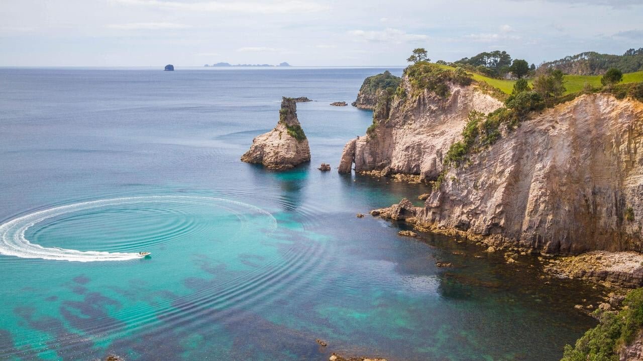 Boat cruising in the calm, turquoise waters of a picturesque bay near Cathedral Cove, Coromandel