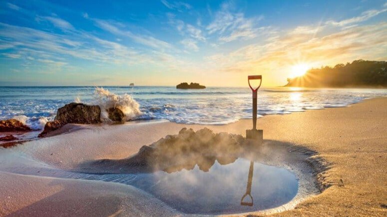 Sunset casting warm golden light over Hot Water Beach’s sandy shores and rock formations