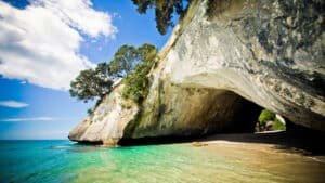 Iconic Hole in the Rock formation with golden sandy beaches and clear blue water on Coromandel Peninsula