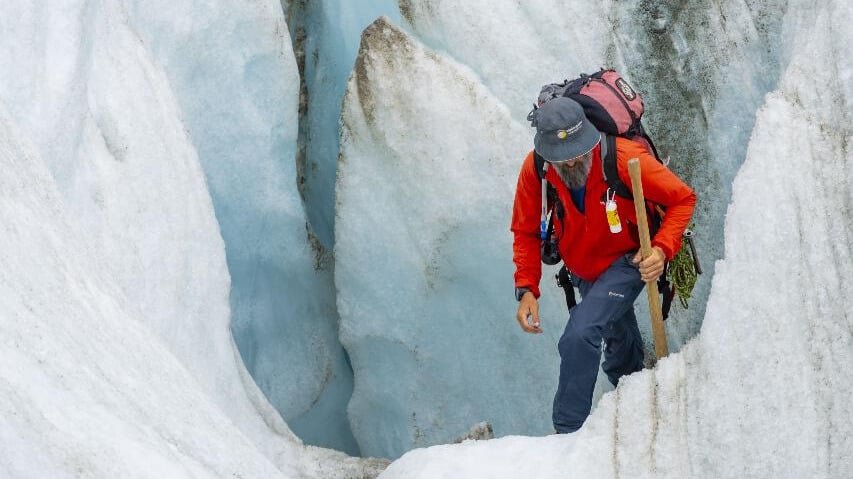 Tour guide tramping out of a brilliant blue ice cave on a helihike of Tasman Glacier from Queenstown