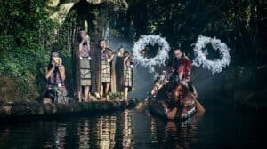 Māori cultural performance in traditional dress beside a carved waka canoe