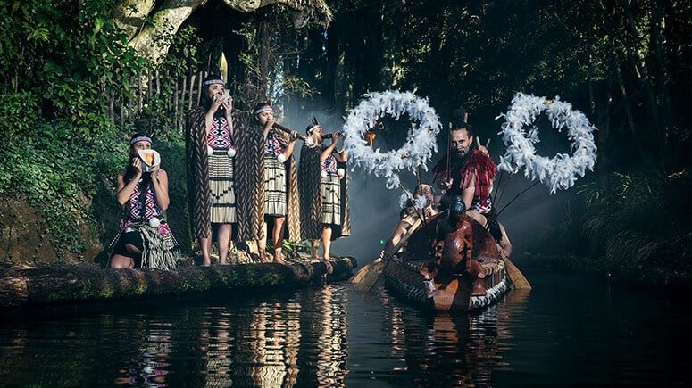 Māori cultural performance in traditional dress beside a carved waka canoe