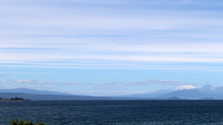 Snow-capped mountain in the distance across a calm New Zealand lake or bay