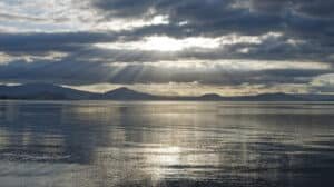 Sunlight breaking through clouds over water with mountain backdrop in New Zealand