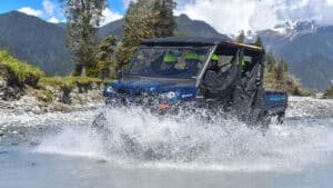 Family driving a 4x4 buggy through a shallow river during an off-road adventure in Franz Josef.
