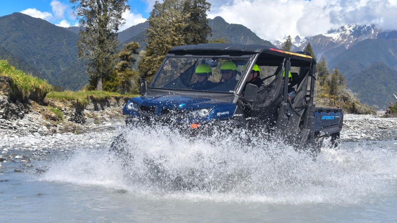 Family driving a 4x4 buggy through a shallow river during an off-road adventure in Franz Josef.