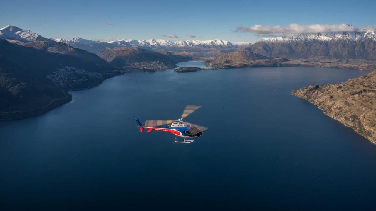 Helicopter flying over a turquoise lake and snow-covered mountains in Queenstown during a heli wine tour.