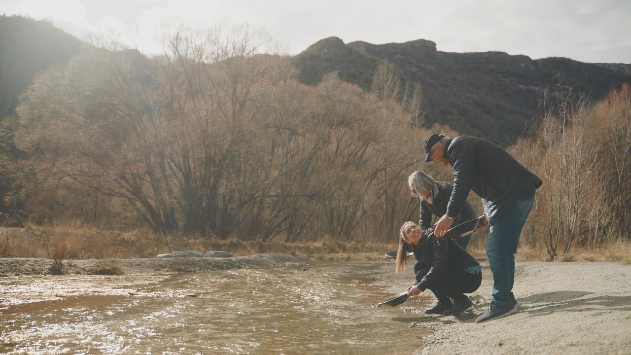Person panning for gold beside a river in Arrowtown during a Queenstown scenic tour.