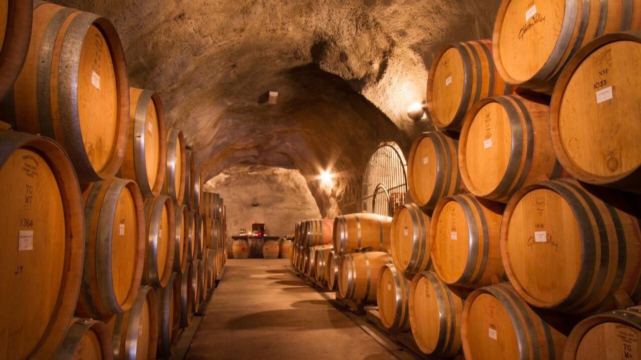 Wine barrels aging in the dimly lit cellar cave at Gibbston Valley Winery during the Queenstown Wine Sampler Tour.