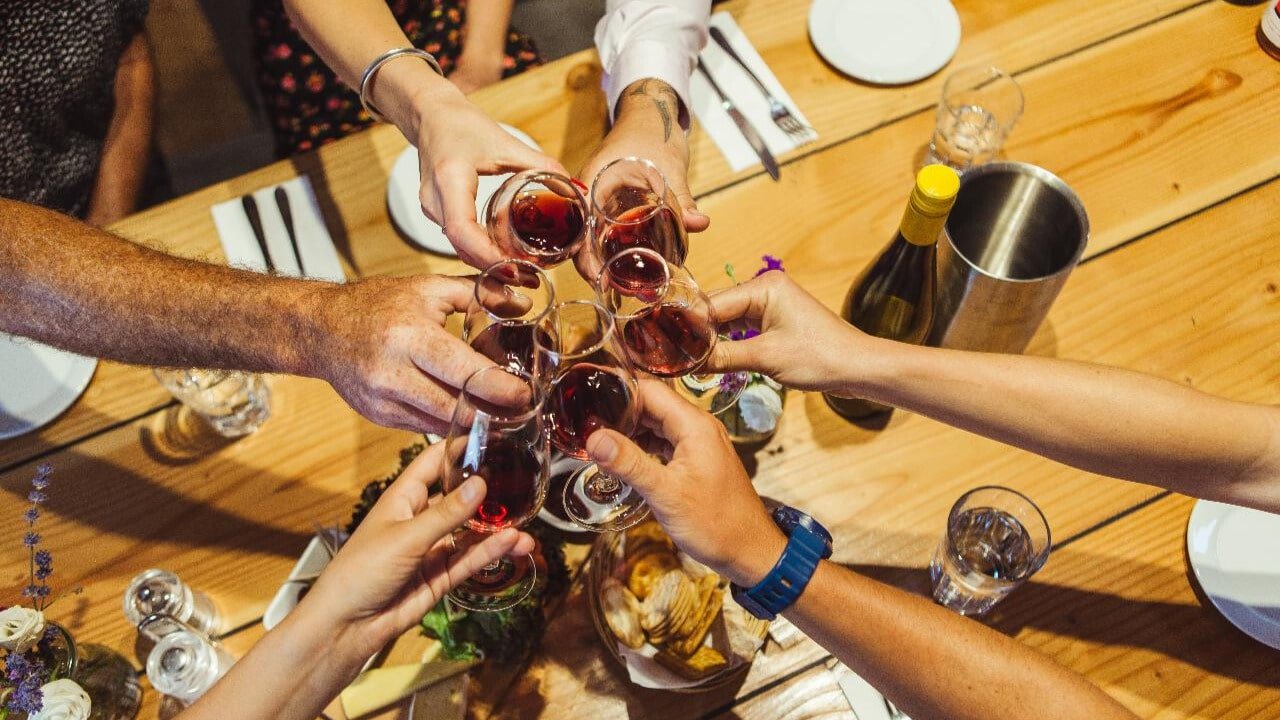 A group raising wine glasses in a toast over a lunch table at Kinross Winery during the Queenstown Wine Sampler Tour.
