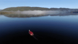 Boat cruising on an incredibly smooth, glass-like lake in Franz Josef surrounded by nature.