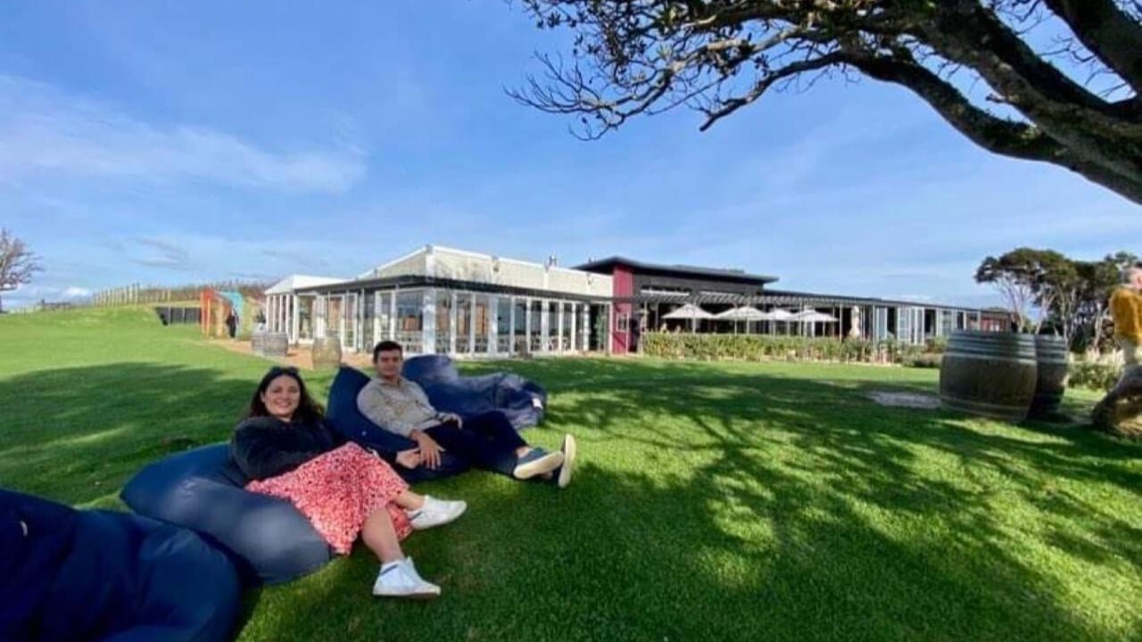 Guests lounging on beanbags under a tree with wine in hand on a sunny Waiheke vineyard lawn
