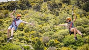 Two people ziplining side-by-side with arms reaching out towards each other on Waiheke Island