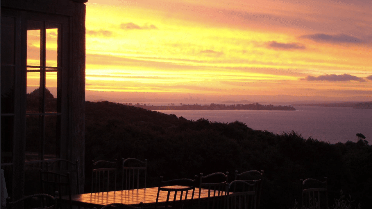 Couple dining outdoors under bright orange sunset skies on Waiheke Island
