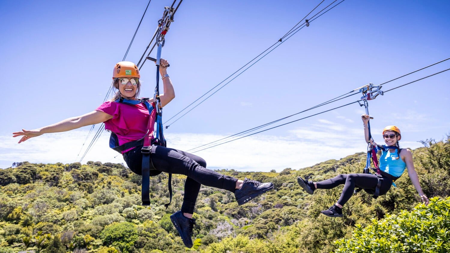 Two people ziplining side-by-side through the forest on Waiheke Island