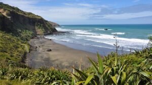 Scenic black sand beach bay along Auckland’s wild west coast with waves gently lapping the shore