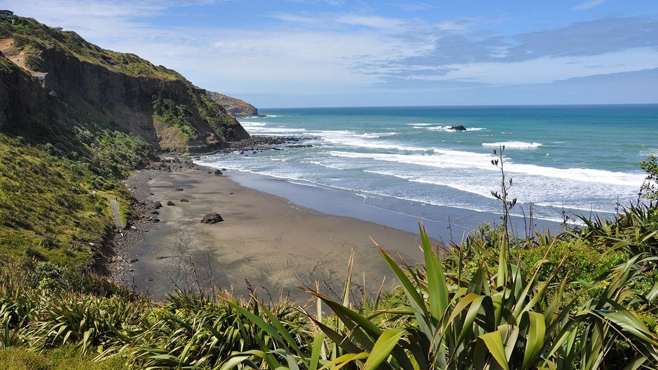 Scenic black sand beach bay along Auckland’s wild west coast with waves gently lapping the shore