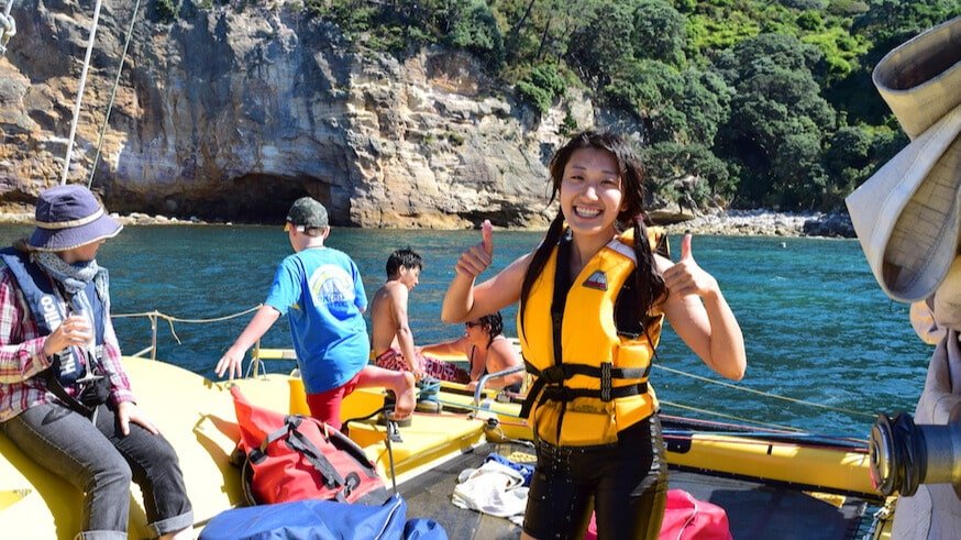 Smiling woman giving two thumbs up on a catamaran cruise from Flaxmill Bay, with kids and bubbles onboard