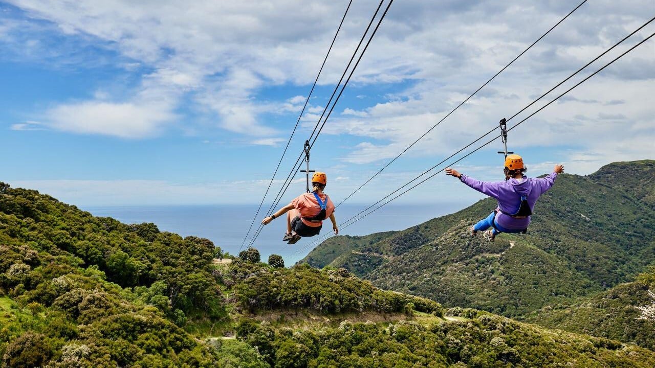Two people racing side by side on parallel ziplines with scenic views in Kaikōura