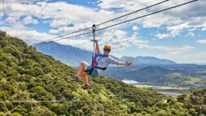 Person waving while ziplining through native forest with breathtaking views in Kaikōura