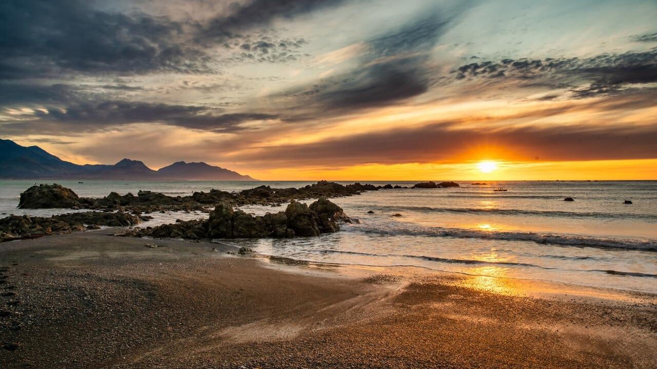 Golden sunset casting warm light over a rocky seashore in Kaikōura during a whale watch and dive small group tour
