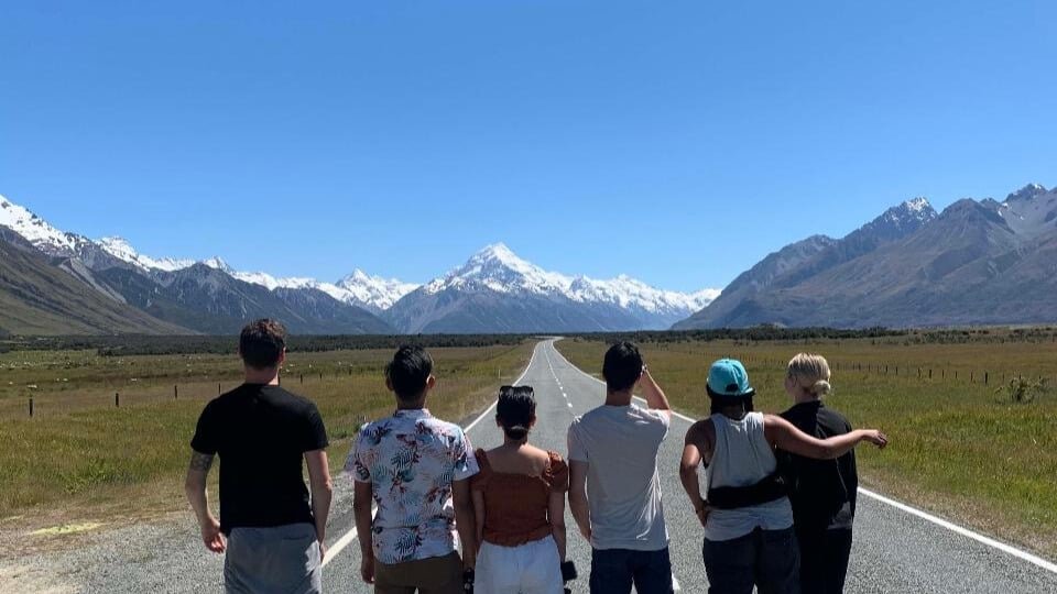 Small group standing on a long straight road leading towards snow-capped mountains on Mount Cook scenic drive tour from Queenstown
