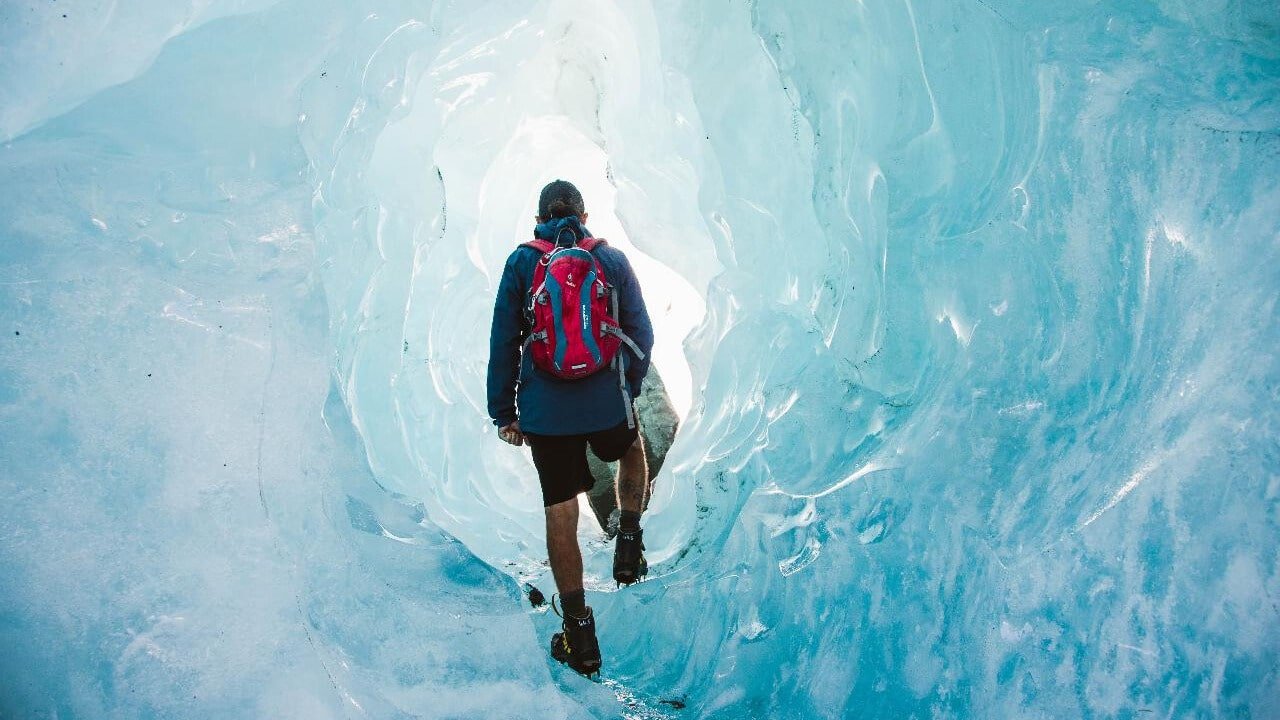 Person tramping through striking blue ice caves on a Mount Cook scenic tour from Queenstown