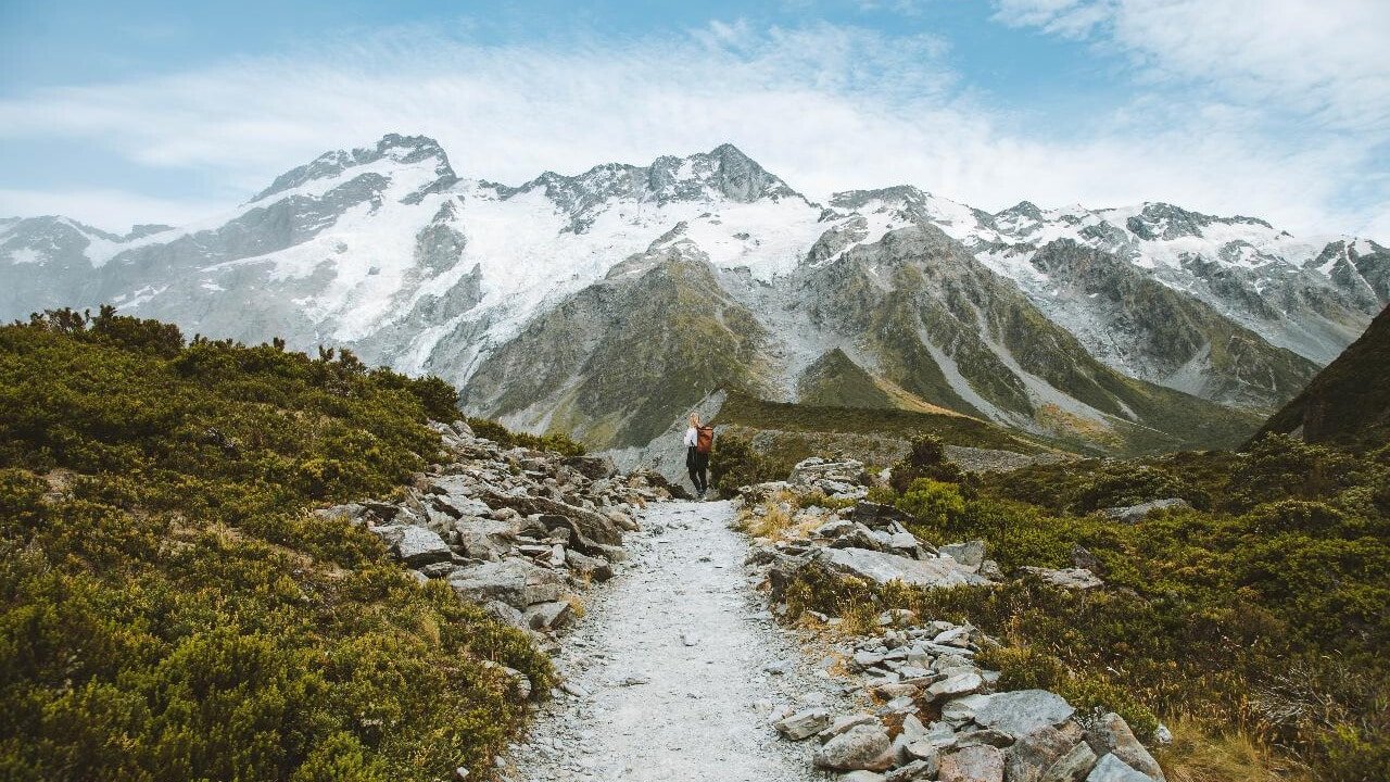 Rocky tramping paths leading toward snowy mountain peaks on Mount Cook scenic tour from Queenstown