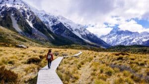 Winding wooden boardwalk through grassy landscape leading toward snowy mountains on Mount Cook tramping track tour from Queenstown